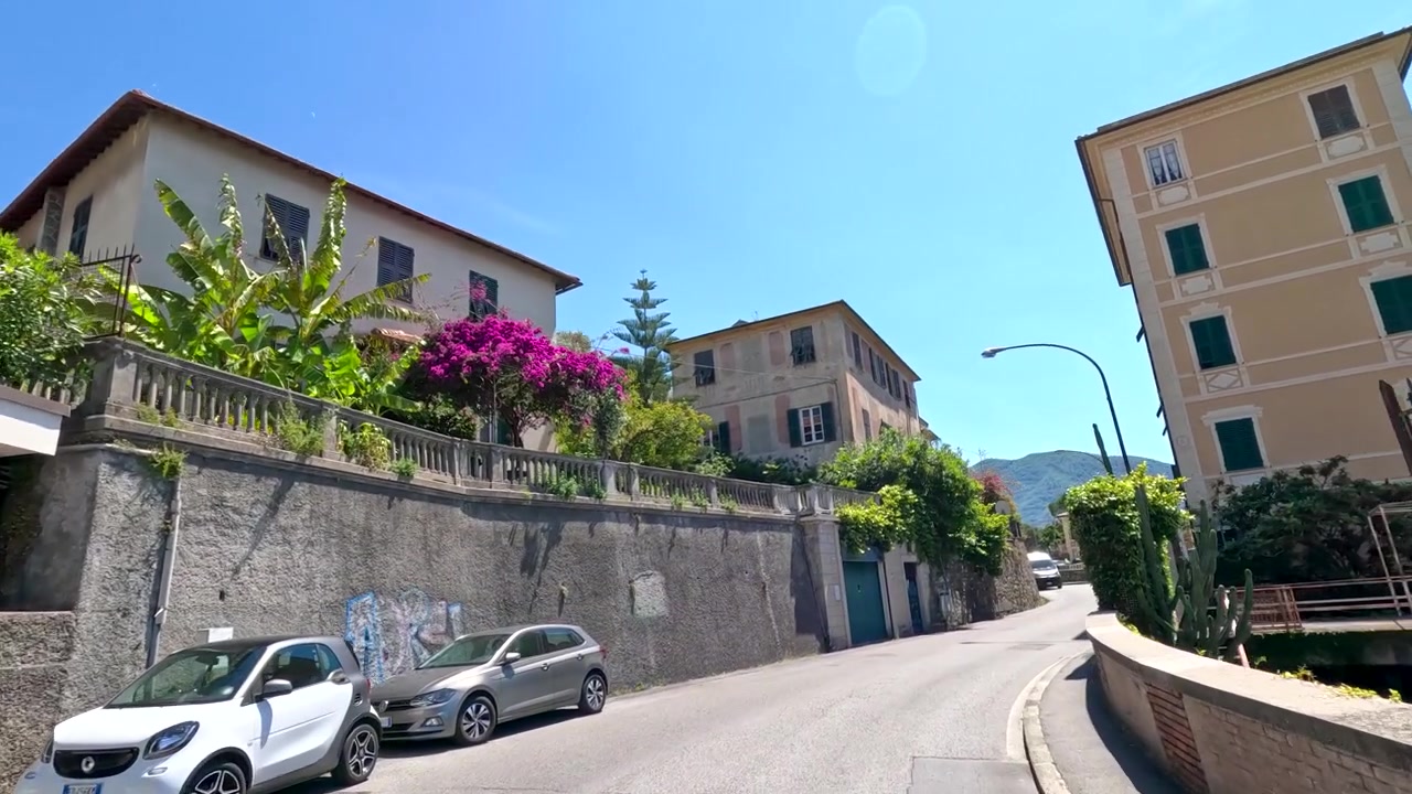 A wide-angle tracking shot moves through a sunny street lined with colorful Italian architecture.