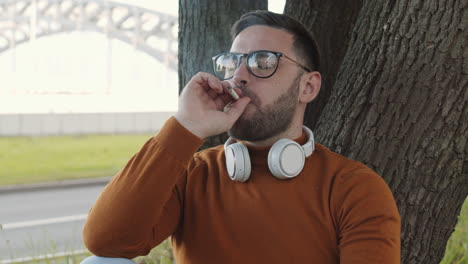 man smoking cigarette leaning on tree