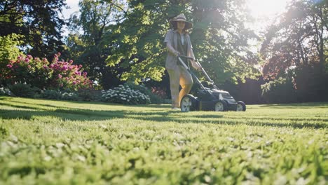 low-angle shot of a person mowing a sunlit garden, capturing a serene, summery vibe
