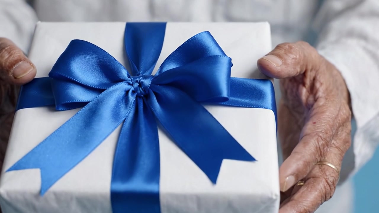 Una persona anziana che tiene in mano una scatola regalo splendidamente incartata con un nastro blu, celebrando momenti speciali e occasioni gioiose con i propri cari.