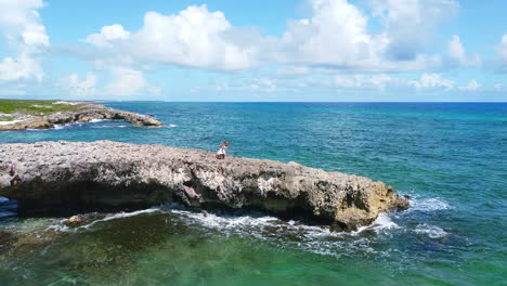 girl in white dress walking on large boulder on cozumel coastline in mexico on sunny day