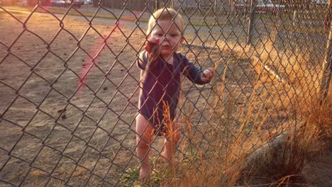 Happy-toddler-boy-stands-looking-through-fence-near-home-plate-playing-with-stick