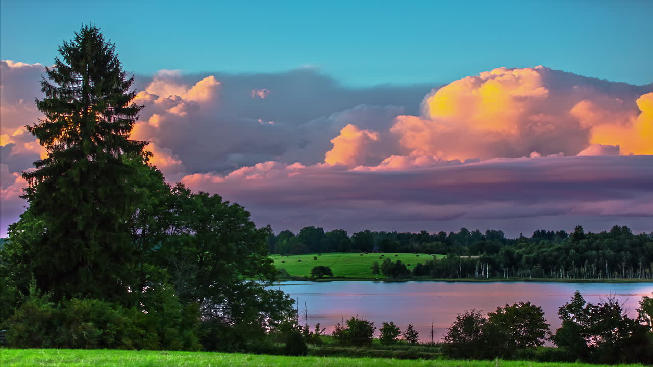 imágenes de timelapse de nubes blancas hinchadas que se mueven rápidamente en un cielo azul claro sobre un paisaje rural con tierras verdes y un lago rodeado de árboles