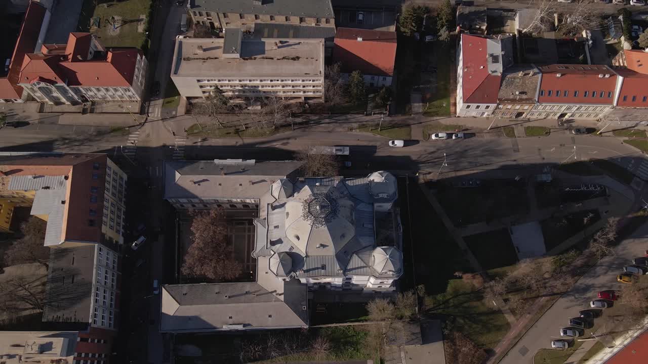 An aerial video of a historic building with an intricate domed roof, surrounded by urban streets and modern buildings. The surrounding area includes roads, parked cars, and green spaces.