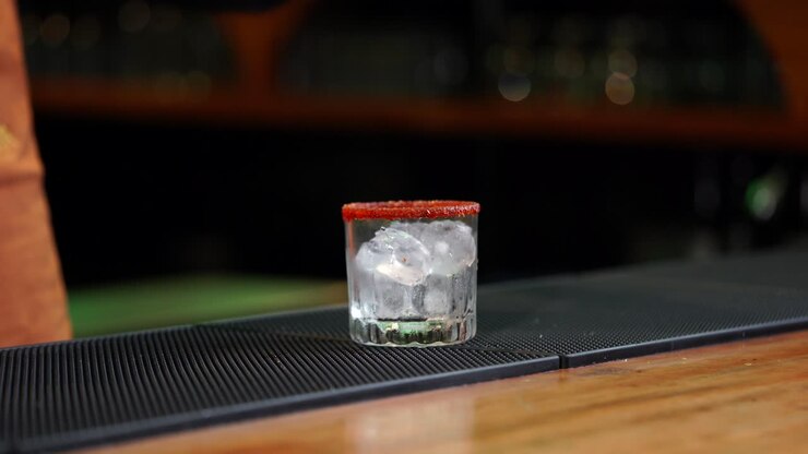 Barman latino serve un cocktail ai frutti rossi da shaker a bicchiere, in un ristorante bar messicano o cantina, con opzioni di mixologia come mojito, shot, mezcal e tequila.