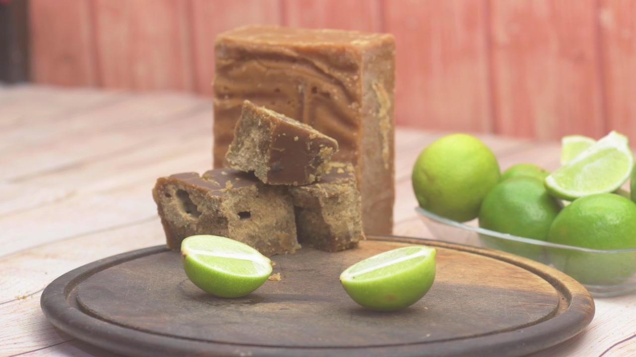 close-up of a hand placing a sliced lime on a rustic wooden board, preparing authentic traditional Venezuelan drink made with unrefined cane sugar panela, fresh lime juice, and water