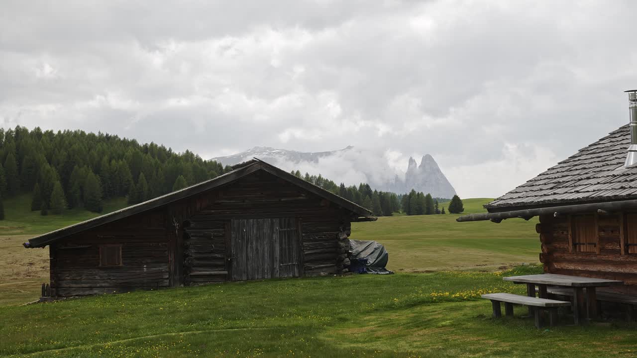 Rustic wooden pasture huts in Alpine meadow with mountain backdrop