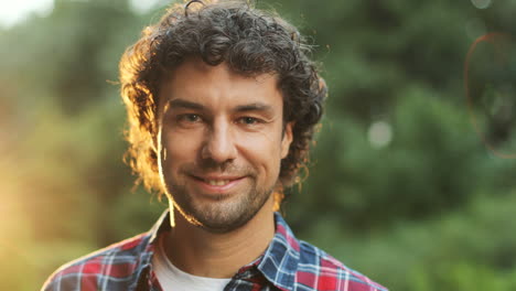 close up portrait of a happy young man turning his head to the camera and smiling. sunshine in the background. blurred background.