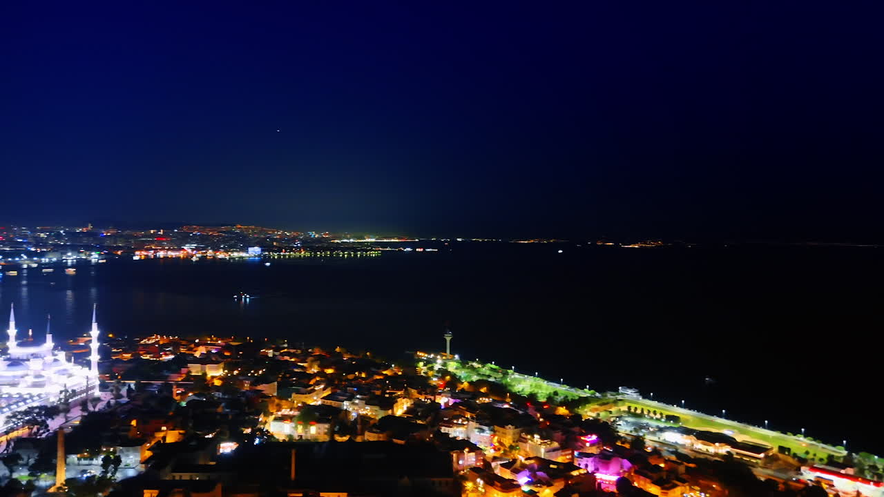 Illuminated scenery of the city divided by the dark waterscape. Boat moves by the sea. Night view of Istanbul, Turkey. Aerial view