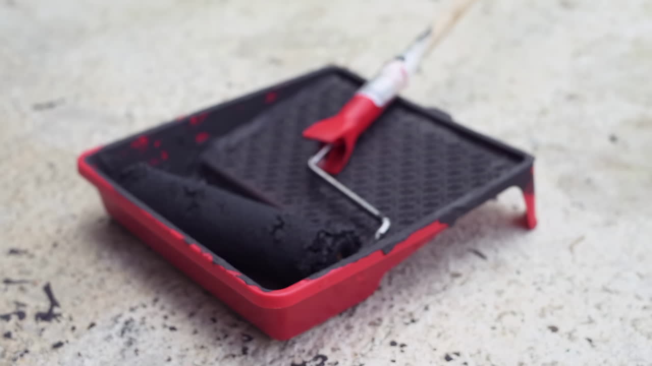 Close up of a roller brush on a red paint roller tray with black dye on it