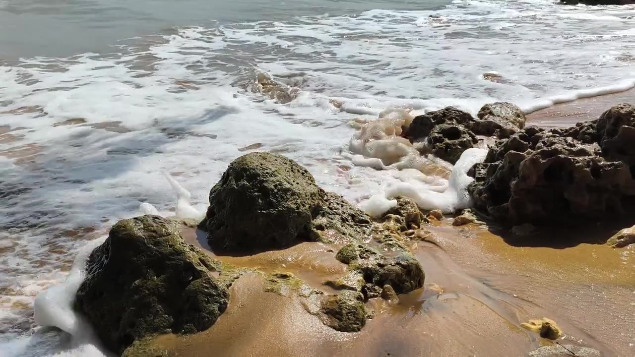 Onde dell'oceano che si infrangono dolcemente su una spiaggia rocciosa e sabbiosa