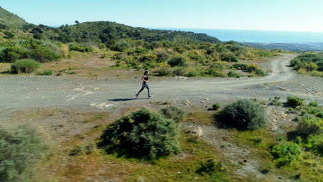 toma de arco aéreo de una mujer rubia trotando en las montañas en un día soleado