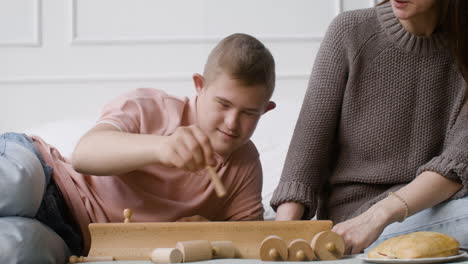 Close-up-view-of-a-boy-with-down-syndrome-and-his-mother-playing-with-wooden-toy-sitting-on-the-bed-in-the-bedroom-at-home