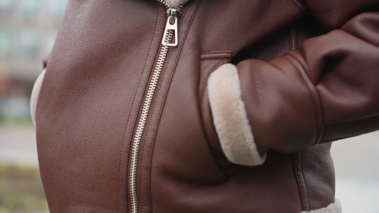 Shot of person's brown shearling jacket with hands tucked into pockets, face not visible, capturing texture and warmth of winter outerwear on cold day with blurred background in soft natural light