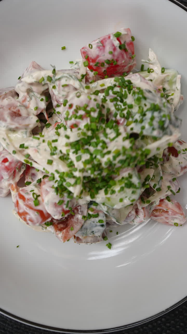 Vertical footage White sauce drizzling over crisp garden salad, ripe tomatoes, fresh cucumbers, juicy onions scattered across plate