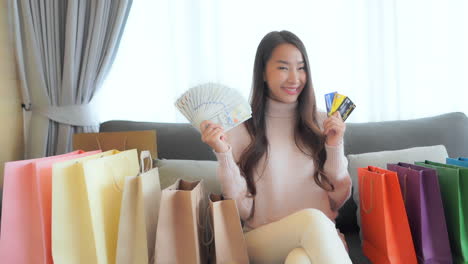 thrilled asian woman posing to camera with a cash dollar money and credit cards