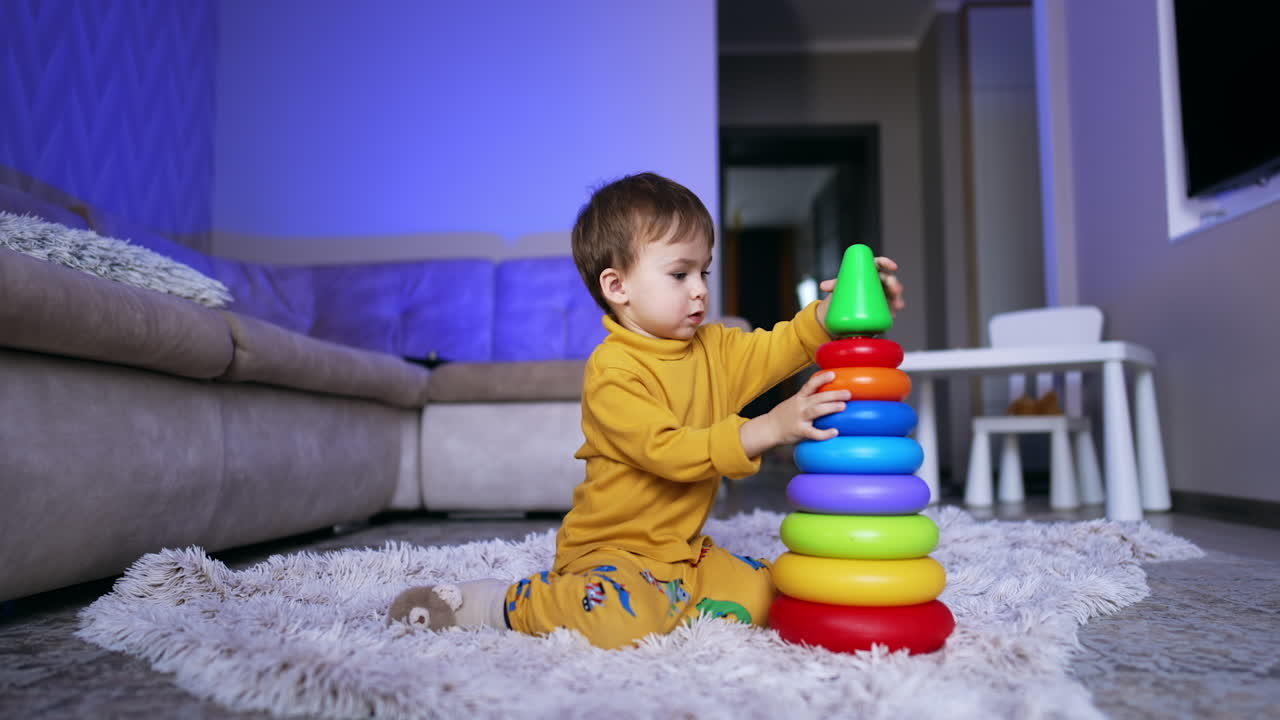 Lovely Caucasian toddler is focused on the colorful toy pyramid. Kid ruins the pyramid and disassembles its parts.