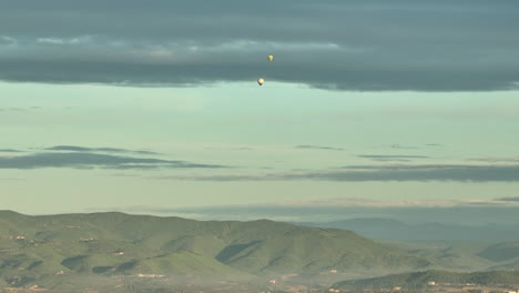 far away view of colorful hot air balloons flying over mountain