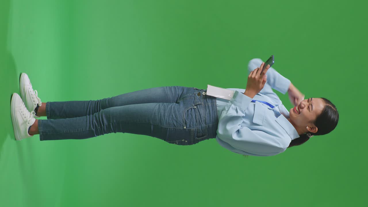 스튜디오의 녹색 화면에서 휴대전화를 사용하여 축하하는 행복한 아시아 사업가 여성의 전체 몸의 측면 시각