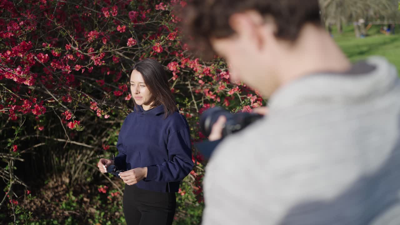 Photographer and female model in sunny day near blooming Chinese Quince shrub