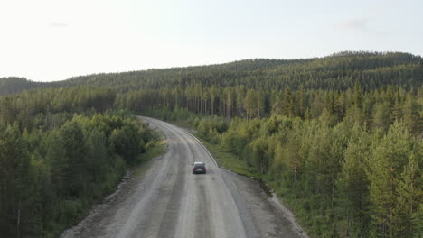 4K-Drohnenaufnahme-Eines-Schwarzen-Autos,-Das-Allein-Fährt-Und-Auf-Einer-Leeren-Landstraße-Durch-Dichten-Wald-Fährt