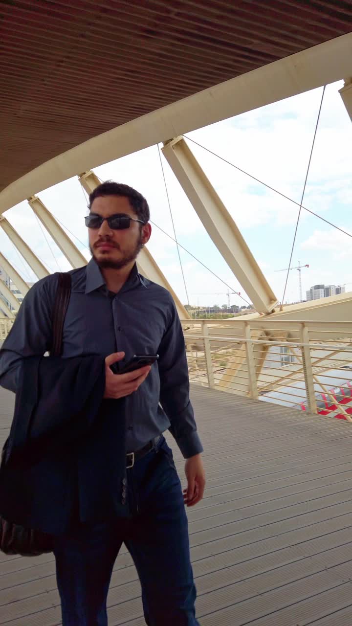 Businessman walking on modern bridge while using smartphone