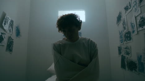 depressed man in straitjacket sitting in seclusion room at psychiatric hospital