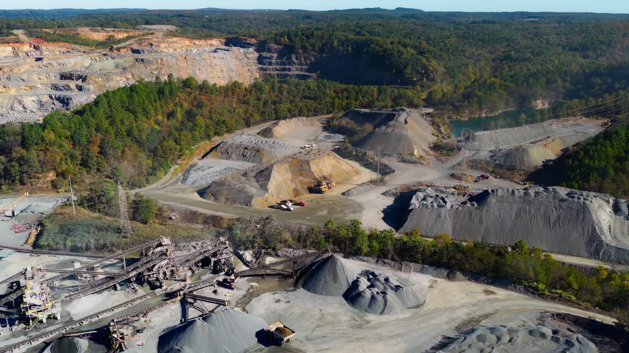 Ampia panoramica aerea di una cava con cave a gradoni e impianto di lavorazione a nastro trasportatore.