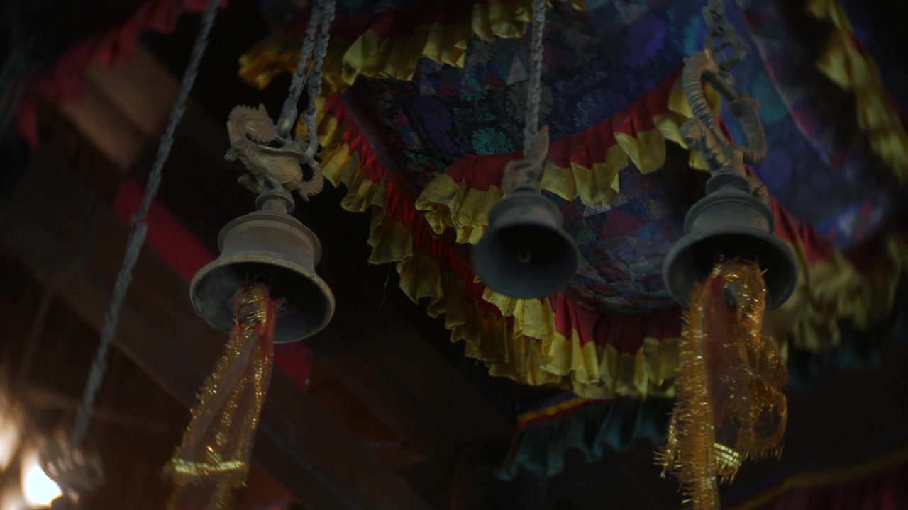 Sinos pendurados em um dossel decorado dentro de um templo, pequenos sinos de metal com borlas suspensos de vigas de madeira. Perspectiva em close-up capturando textura, movimento e decoração religiosa tradicional