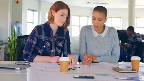 front view of young caucasian female executives discussing over blueprint in modern office 4k