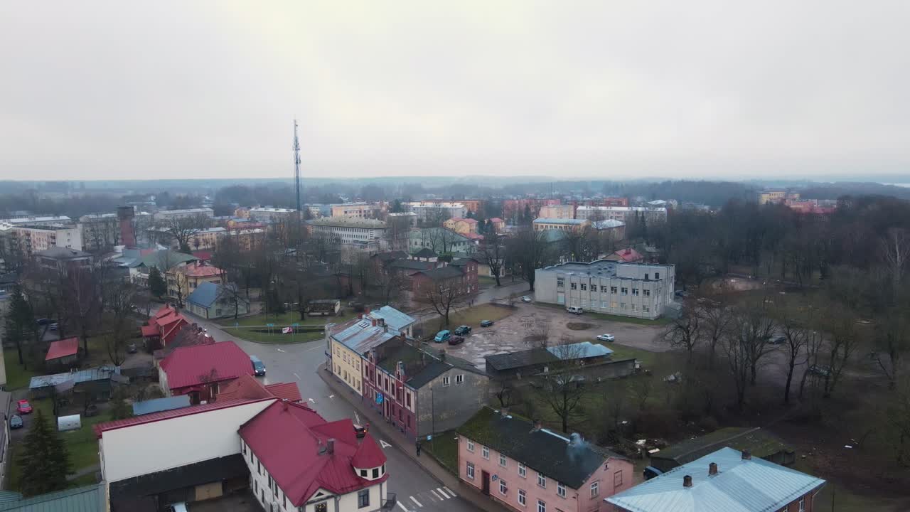 Aerial photo of Balvi city bathed in warm sunset light, featuring urban buildings, parking lots, and a snow-dusted landscape. A peaceful winter scene.