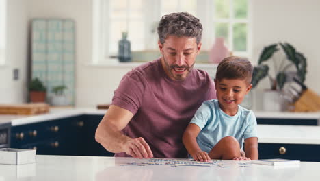 Mature-Father-At-Home-In-Kitchen-With-Son-Doing-Jigsaw-Puzzle-Together