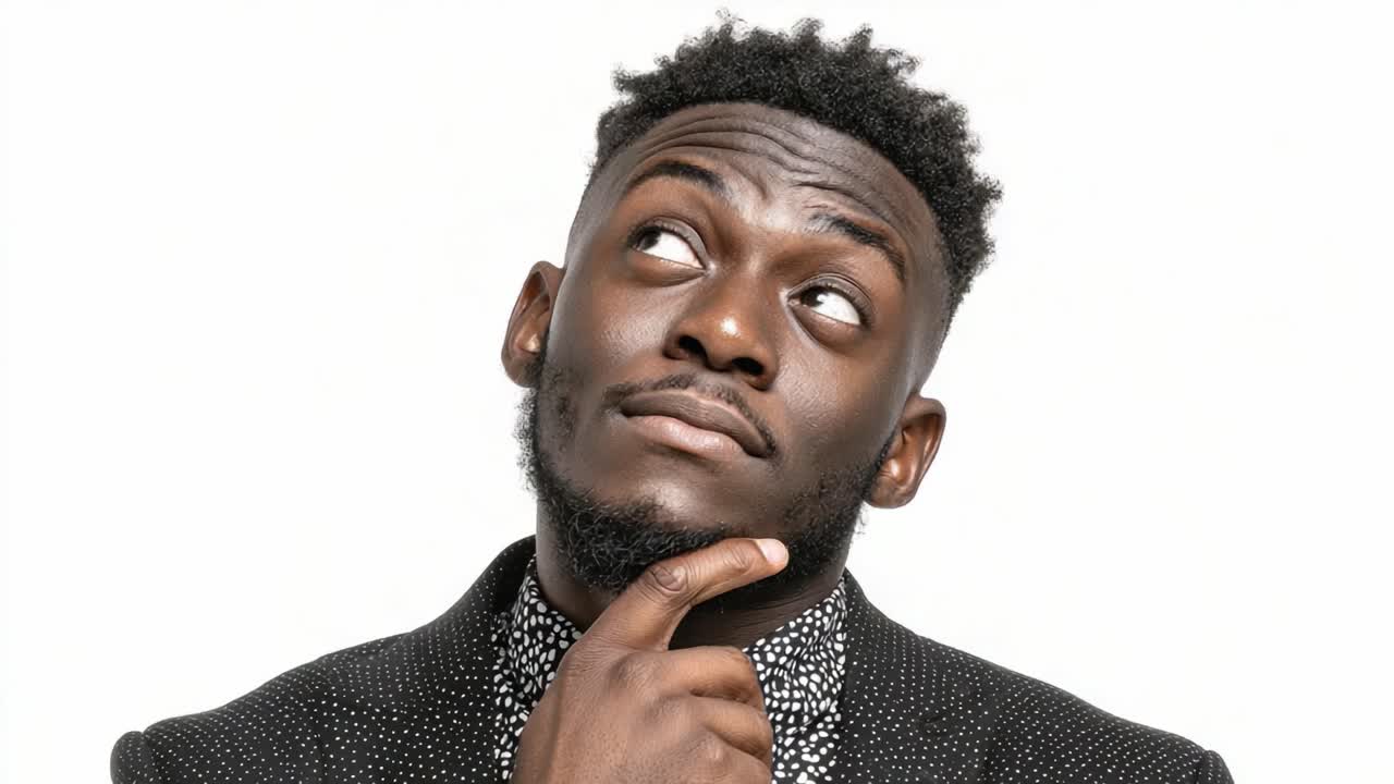A young man in a stylish outfit expresses contemplation and confidence, with a thoughtful pose in a studio setting, capturing a moment of reflection and charisma
