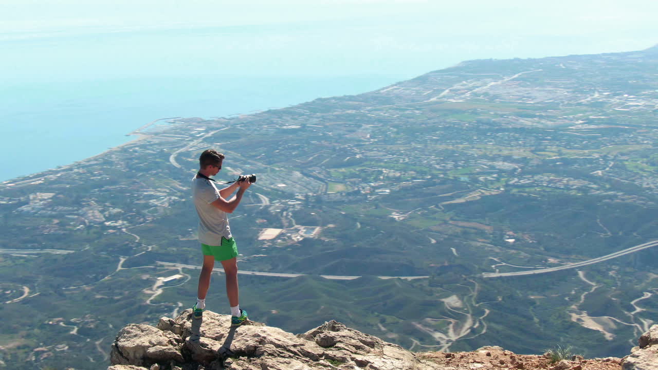 disparo de arco lento de un excursionista masculino tomando fotos de marbella desde la cima de la montaña la concha, mientras sus amigos miran