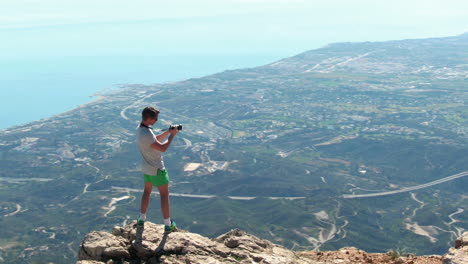 slow arc shot of male hiker taking photos of marbella from top of la concha mountain, while his friends are watching