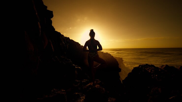 Woman practicing yoga at sunset on a rocky coastline