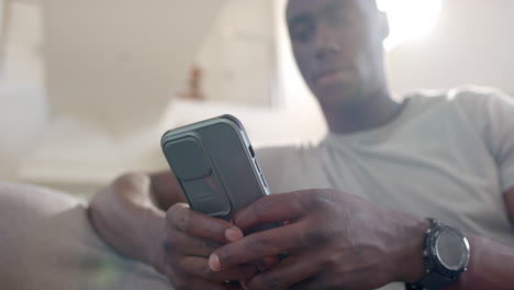 Happy-african-american-male-soldier-using-smartphone-and-laughing-in-sunny-living-room,-slow-motion