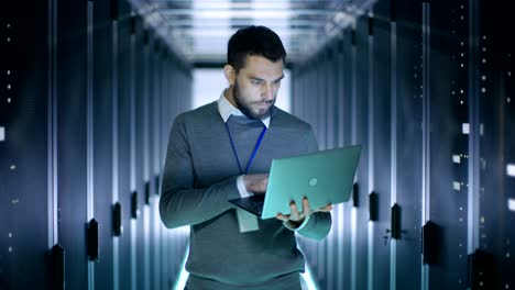 un ingeniero trabaja en una computadora portátil en un gran centro de datos. se ven filas de servidores de rack.