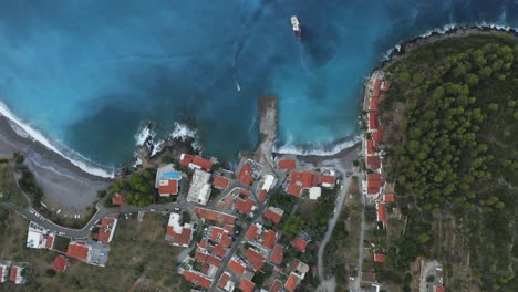 a birds eye view of a coastal village in lakonia, greece with a small boat approaching