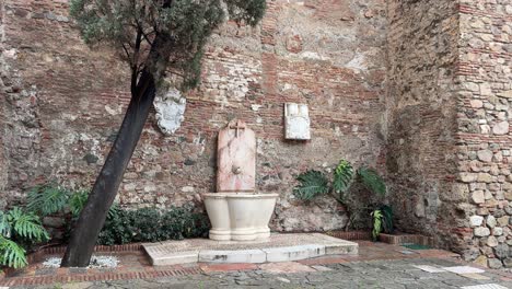 water fountain next to alcazaba castle walls with a cross malaga spain