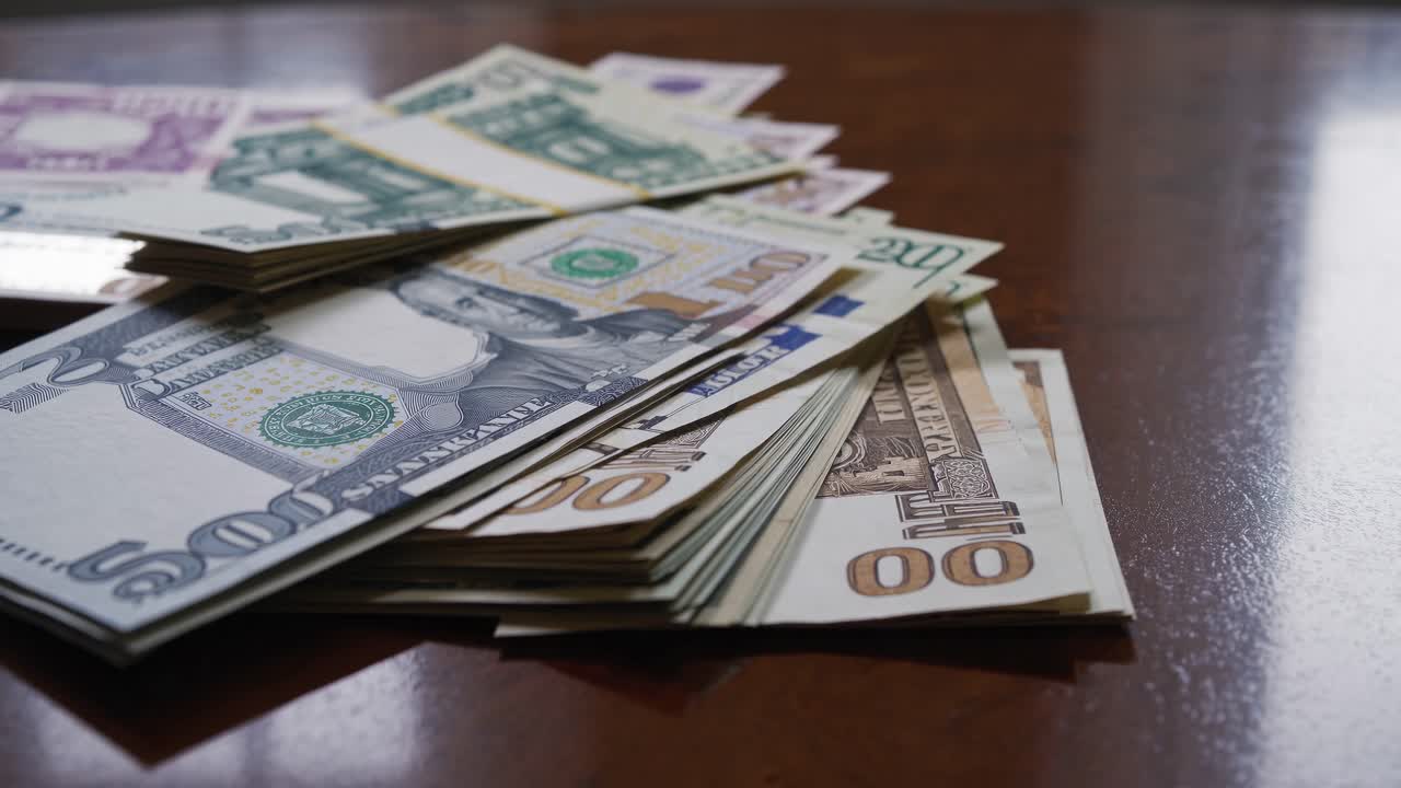 Low-angle shot of various currency stacks on a wooden table, capturing a financial theme suitable