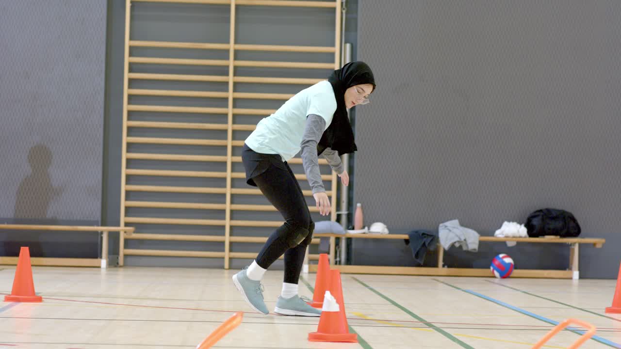 Indisk kvinnelig utøver med hijab starter gymøvelse, hopper over hekk, vever mellom kjegler, griper volleyball