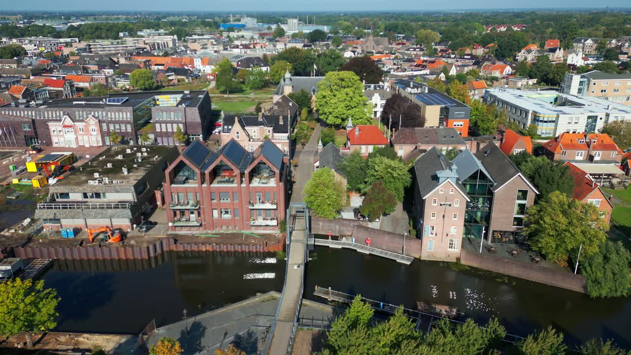 Elevated drone view over Coevorden canal showing pedestrian bridge, modern residential blocks, and historic urban surroundings. Location: Coevorden, Drenthe, Netherlands