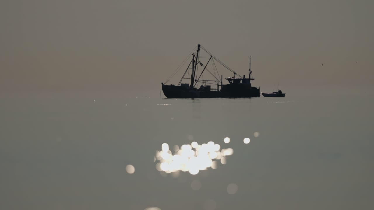 Moody sunset light dance on ocean surface, abstract silhouette of fishing vessel
