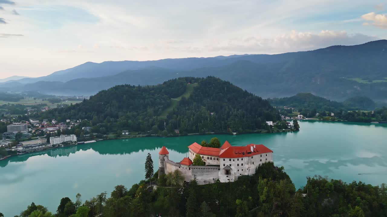 Castello di Bled che domina il tranquillo Lago di Bled, Slovenia. Ripresa aerea parallax con drone, splendida destinazione di viaggio all'alba, 4K cinematografico.