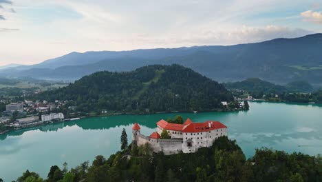 Castillo-Sangrado-Con-Vistas-Al-Tranquilo-Lago-Sangrado-Eslovenia,-Disparo-De-Drones-De-Paralaje-Aéreo,-Hermoso-Destino-De-Viaje-Amanecer-Temprano-En-La-Mañana,-Cine-4k