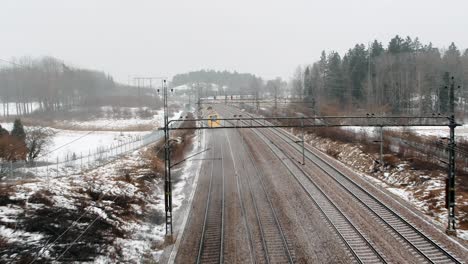 toma aérea de un tren de alta velocidad, arlanda express pasando bajo un dron en un paisaje industrial e invernal que se dirige hacia la terminal de la ciudad de estocolmo