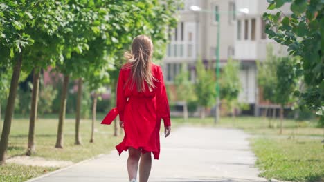 back view of a woman in summer. young female in red dress with long hair is walking on the street to the building in the city.slow motion.