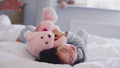 familia con dos padres en la cama en casa jugando con su hija y su juguete blando