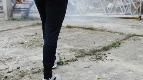 rear view of caucasian man in sportswear hitting a punching bag outdoors an abandoned factory on a cloudy morning